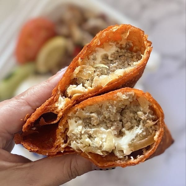 Hand holding a deep-fried empanada, cut open to reveal savory meat and creamy cheese filling.