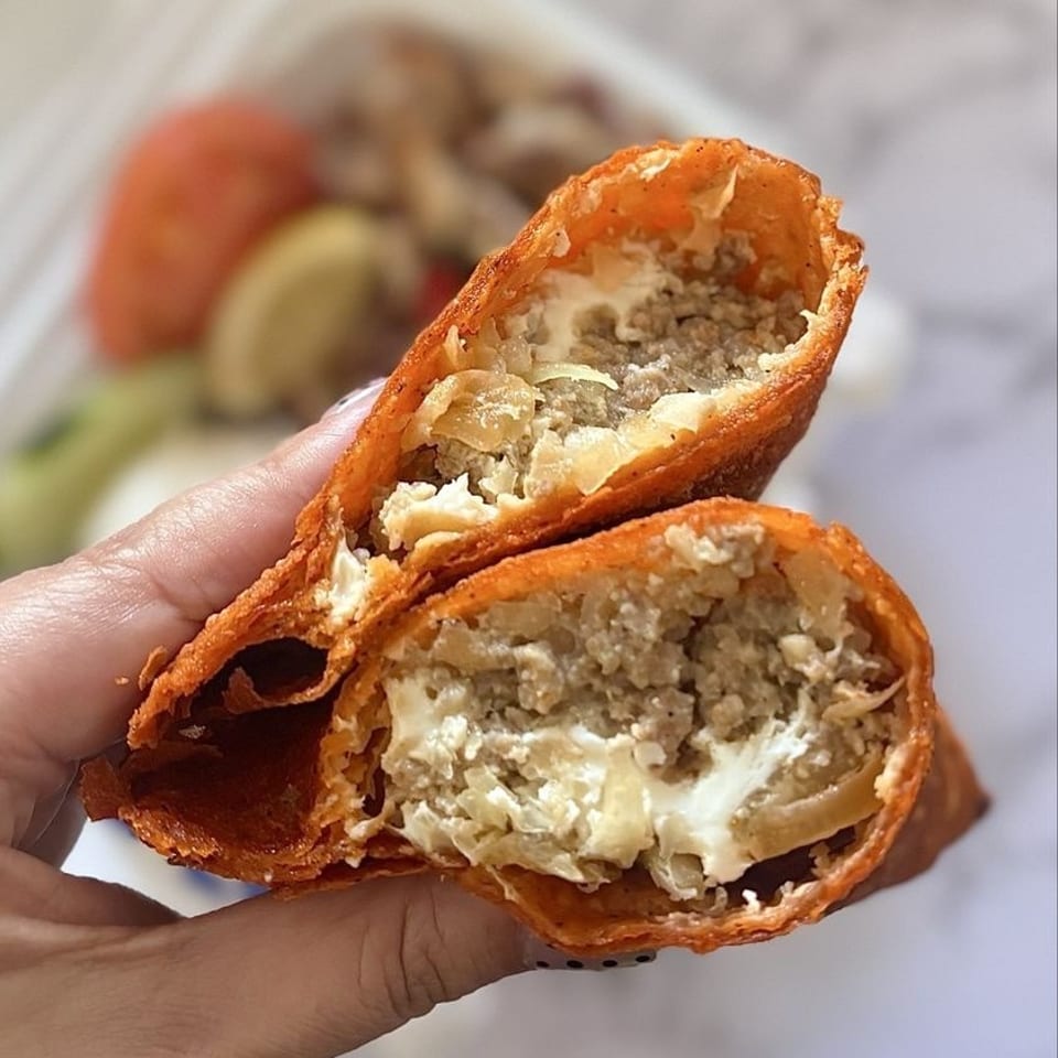 Hand holding a deep-fried empanada, cut open to reveal savory meat and creamy cheese filling.