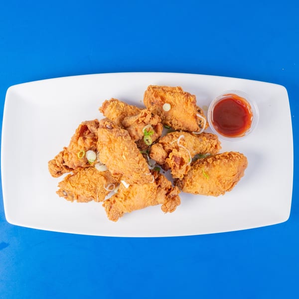 Crispy fried chicken wings with sliced green onions and a side of red dipping sauce on a white plate.