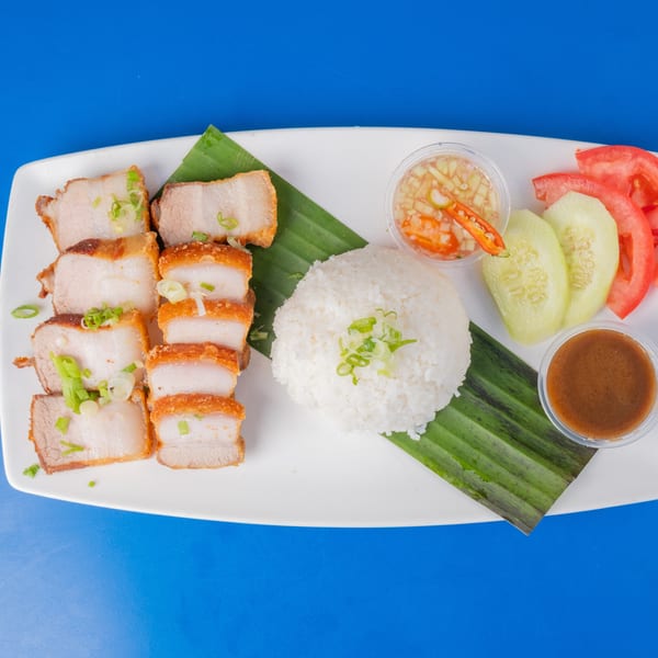 Crispy pork belly slices with rice, cucumber, tomato, and two dipping sauces on a white plate.