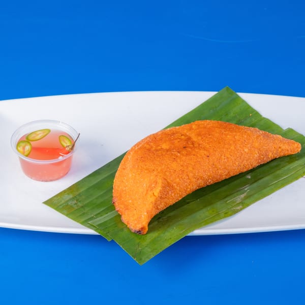 A golden-brown empanada on a banana leaf with a side of pink sauce and sliced peppers.