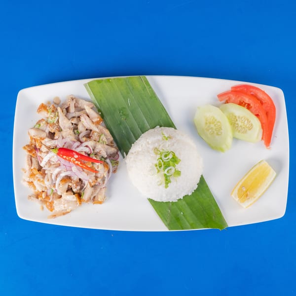 Crispy sisig with rice, cucumber, tomato, and lemon on a white plate with a banana leaf.