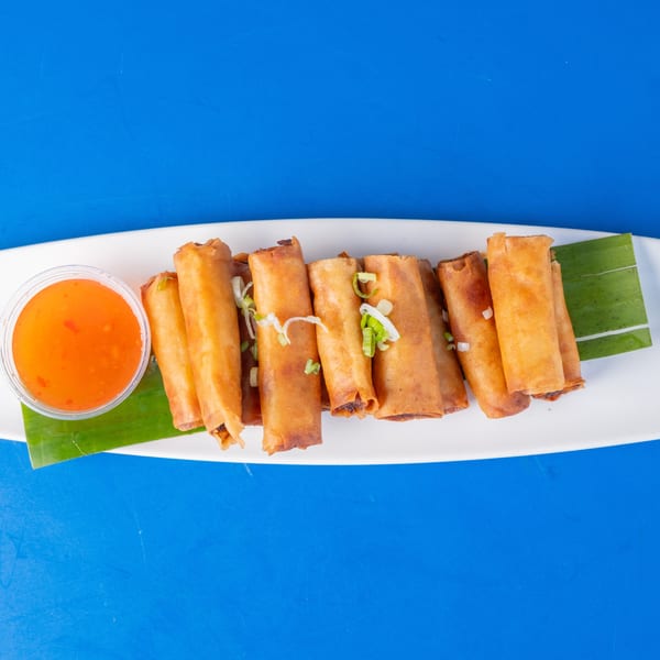 Crispy golden spring rolls with green onion garnish and sweet chili dipping sauce on a white plate.